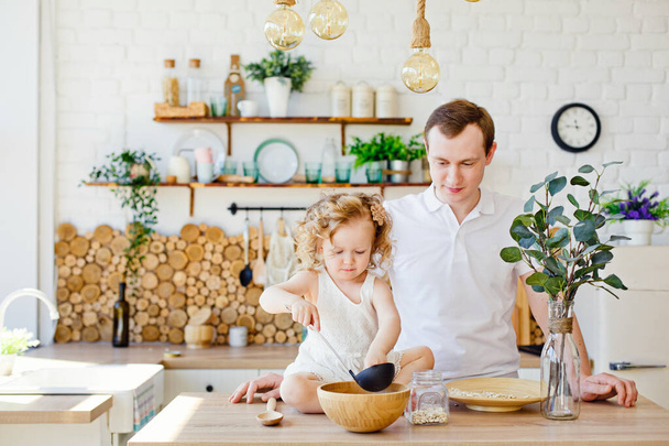 Καυκάσιος πατέρας και κόρη, αστείος πατέρας και κορίτσι αγκαλιάζουν και μαγειρεύουν μαζί στην κουζίνα σε μια φωτεινή κουζίνα, τον τρόπο ζωής και την Ημέρα του Πατέρα, ανύπαντροι γονείς - Φωτογραφία, εικόνα
