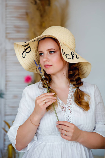 Portret van een charmant lief meisje met lang verzorgd haar, gevlochten in vlechtjes met een hoed in de stijl van de Provence. - Foto, afbeelding