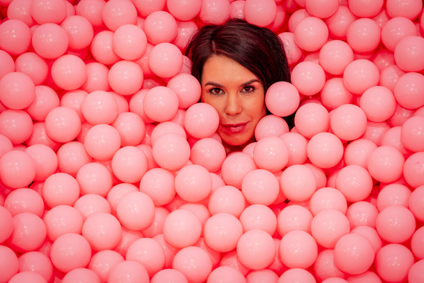 Een prachtig Aziatisch model speelt in een kleurrijke kamer met een enorme hoeveelheid plastic ballen - Foto, afbeelding