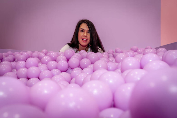 A beautiful asian model plays in a colorful room with a huge amount of plastic balls - Photo, Image