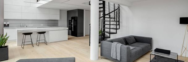 Panorama of elegant loft apartment with white kitchen open to contemporary living room and black stairs to next floor - Photo, Image