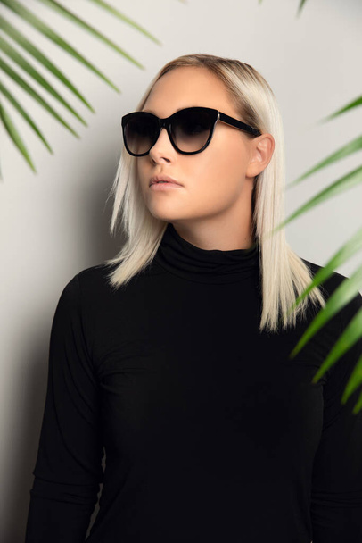 Profiel van een mooie vrouw met een zonnebril verstopt achter tropische palmbladeren - Foto, afbeelding