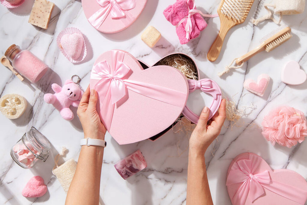 Top view of pink colored heart shaped gift boxes with homemade bath supplies, marshmallows and body care cosmetics products for woman on white marble background. Concept of Christmas charity gifts. - Foto, imagen