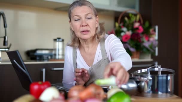 Senior γυναίκα μαγείρεμα με τη βοήθεια της συνταγής στο laptop. - Πλάνα, βίντεο