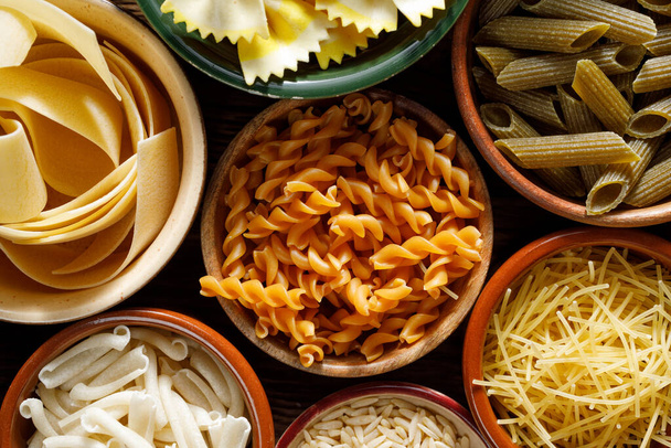 Verschillende soorten pasta in een schaal op een zwarte achtergrond, van dichtbij bekeken - Foto, afbeelding