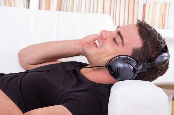 przystojny mężczyzna odpoczynku na kanapie, słuchanie muzyki w słuchawkach - Zdjęcie, obraz