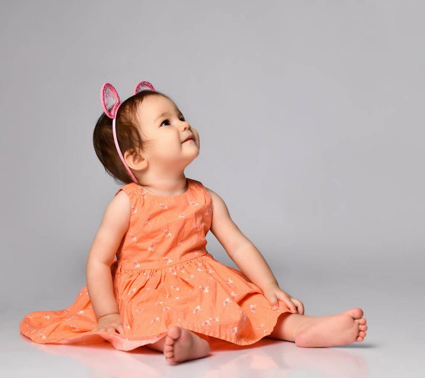 Little girl dressed in a dress and a hoop with ears sitting on a gray background in the studio. - Photo, image