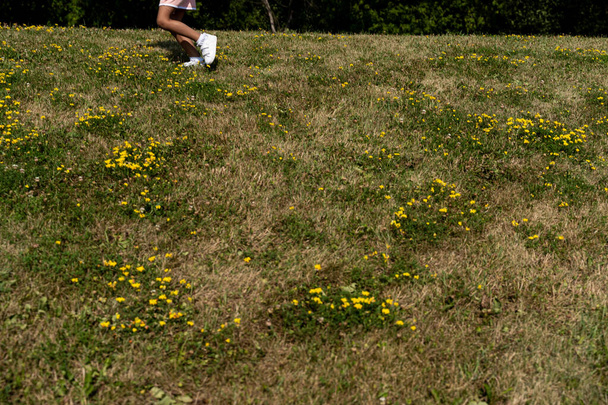gedeeltelijk zicht op benen van jong meisje in roze jurk en hardlopen in een park gezien van achteren - Foto, afbeelding