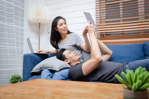 Aasialainen nuori pari Istu ja rentoudu sinisellä sohvallaan kotonaan lomien aikana. Perhekonsepti, kotona työskentely. kopioi tila - Valokuva, kuva