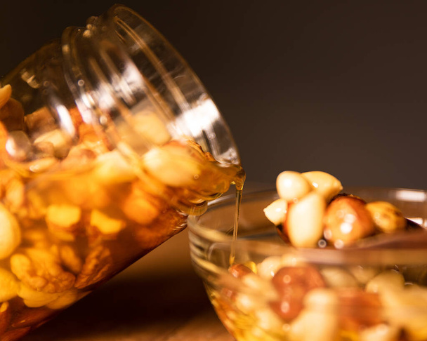 Med smíchaný s ořechy, semena vylitá z průhledné sklenice do skleněné misky. Fotografie zátiší. - Fotografie, Obrázek