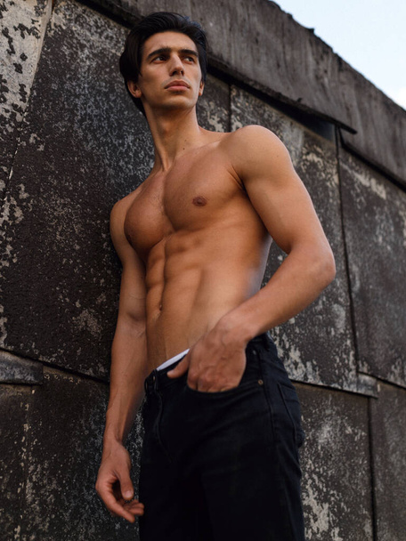 Jeune homme attrayant avec torse nu près du vieux mur noir. Homme sain et sportif. Vue verticale. - Photo, image