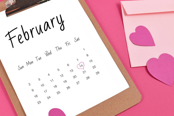 February calendar sheet with Valentine's Day on the 14th marked with heart surrounded by hearts and love letter on pink background - Fotografie, Obrázek