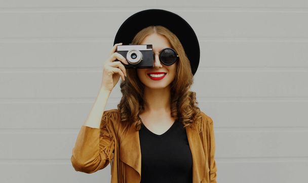 Portrait of happy smiling young woman photographer with vintage film camera wearing a boho style on a gray background - Foto, Bild