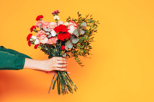 Beautiful mix bouquet and different flowers holding female hands on a yellow background - Foto, afbeelding