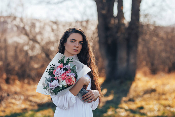 Νεαρή γυναίκα με λευκό φόρεμα που κρατά ένα όμορφο μπουκέτο τριαντάφυλλα - Φωτογραφία, εικόνα