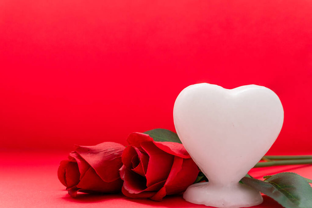 white heart shaped candle with two roses on the side, copy space, with red background, for valentine's day - Φωτογραφία, εικόνα