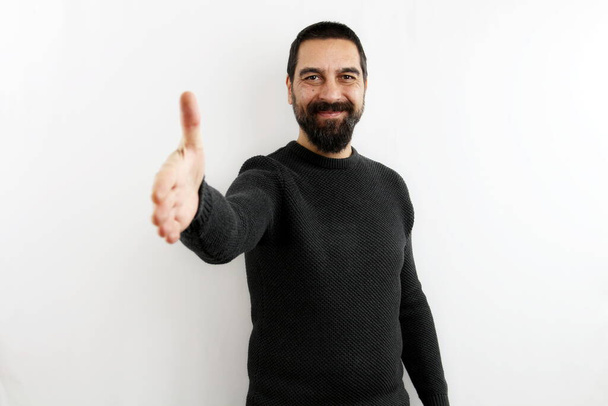 Smiling young bearded man on isolated white background smiling stretches out his arm by opening his hand in greeting. Greet, shake hands - Photo, Image