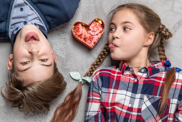 Hermana divertida y hermano sobresalen lenguas el uno al otro, adolescentes felices y sonrientes con galletas en forma de corazón - Foto, imagen