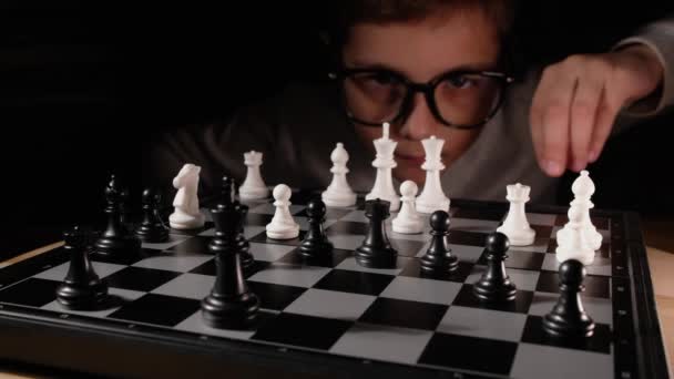 Παιδί που παίζει σκάκι στο τραπέζι. Μικρό αγόρι με γυαλιά ανάπτυξη στρατηγικής σκάκι, να παίξετε επιτραπέζιο παιχνίδι με το φίλο. - Πλάνα, βίντεο