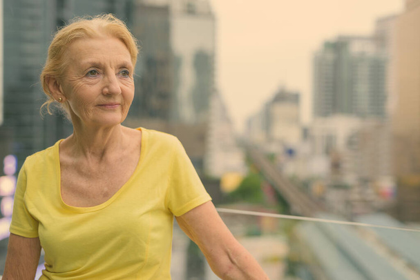 Красивая пожилая женщина с светлыми волосами с видом на город - Фото, изображение