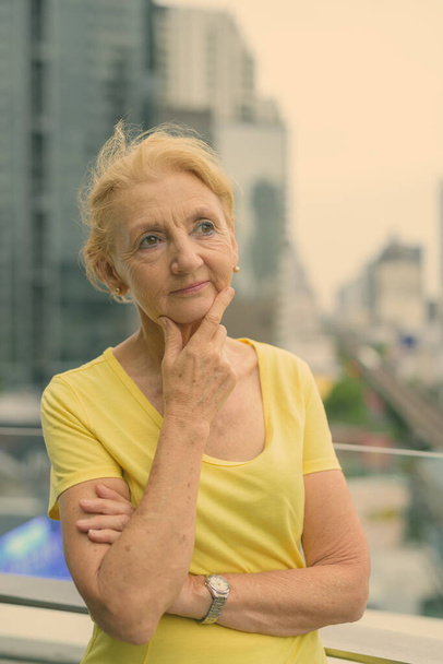 Красивая пожилая женщина с светлыми волосами с видом на город - Фото, изображение