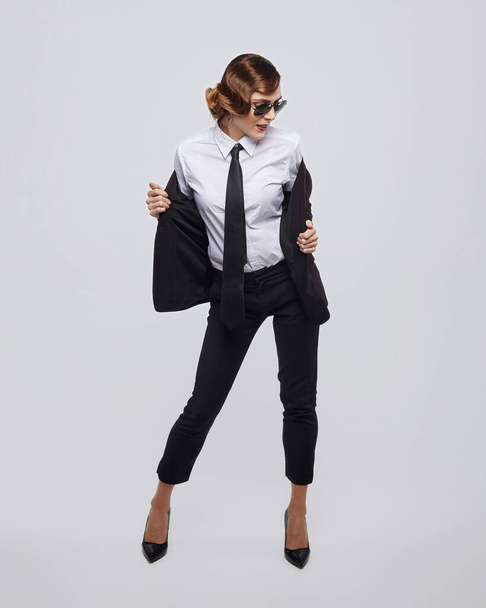 attractive woman with a retro hairstyle poses in a men's suit and sunglasses - Фото, изображение
