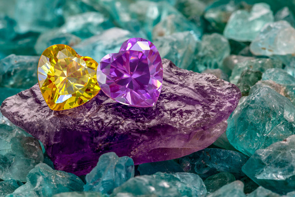 生のスカイブルーの宝石に置かれたイエローハートダイヤモンドとレッドルビーハートダイヤモンド。ハート形のジュエリーはバレンタインデーのために素敵なプレゼントです - 写真・画像