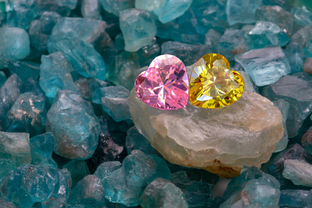Różowe i żółte serca są umieszczone razem na surowym fioletowym kamieniu ametyst pośród surowego nieba niebieskie kamienie. - Zdjęcie, obraz