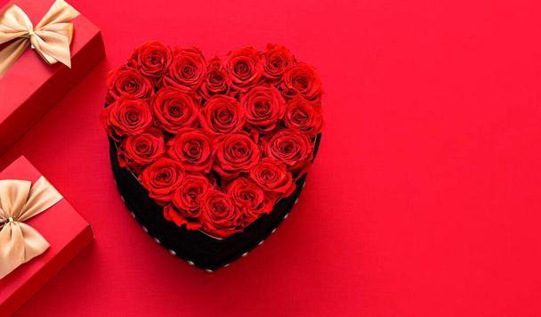 Valentine's day. Red heart made of roses. Red ackground with Valentines gifts decor. Top view with copy space. Minimalism. Flower box witch roses. Happy Valentines. - Photo, Image