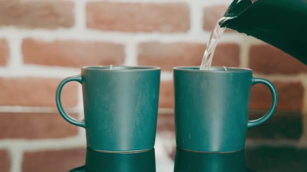 Making tea for two people. Pouring hot water into green tea cups standing on a mirrored love surface on a red brick wall background. Morning tea for two early in the morning. - Footage, Video