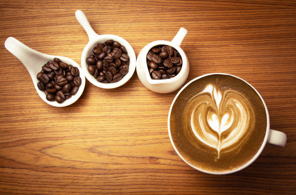 Cappuccino chaud avec grains de café torréfiés sur un fond en bois et espace libre - Photo, image