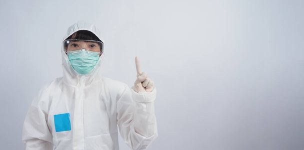 ジェスチャー博士。PPEスーツや個人保護機器のアジアの女性医師ジェスチャーと指摘します。白い医療用ゴム手袋。流行性コロナウイルスを保護するゴーグルグラスと緑のN95マスク. - 写真・画像