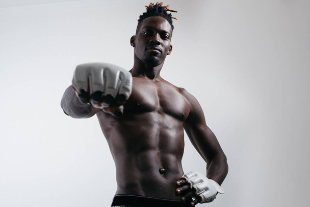 A confident young African boxer in boxing gloves reaches out and stares into the camera while standing isolated on the grey - Φωτογραφία, εικόνα