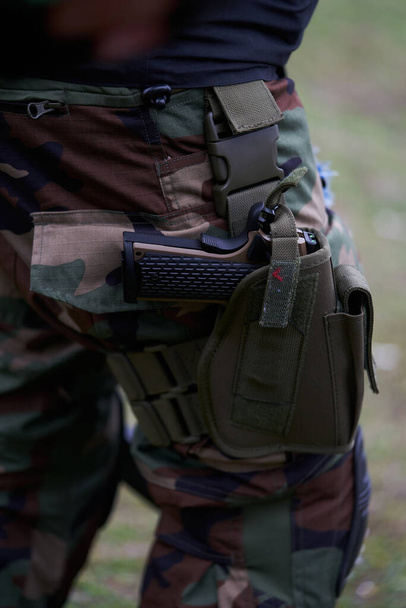 Κοντινό πλάνο πιστολιού σε θήκη στο πόδι στρατιώτη με στολή καμουφλάζ. - Φωτογραφία, εικόνα