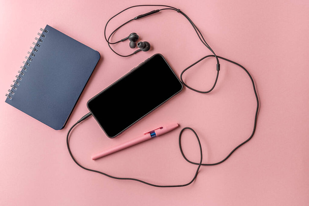 notepad, pen and smartphone with headphones on a pink surface, top view, mock up - Photo, image