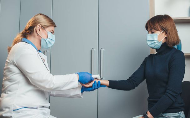 Médecin blonde senior mesure la température sur la main des patients à l'aide d'un thermomètre électrique au bureau de travail - Photo, image