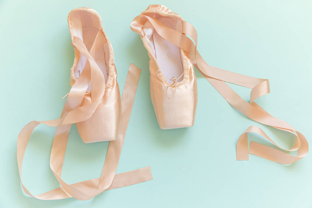 New pastel beige ballet shoes with satin ribbon isolated on blue background. Ballerina classical pointe shoes for dance training. Ballet school concept. Top view flat lay copy space - Photo, Image