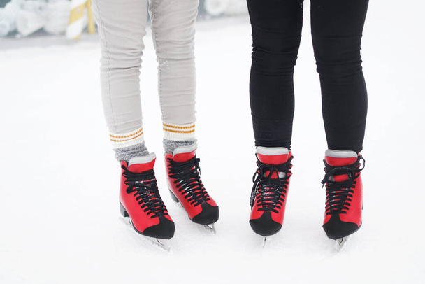 Close-up of friends legs standing in red skates on the ice. Winter activities. Winter entertainment background - Photo, Image