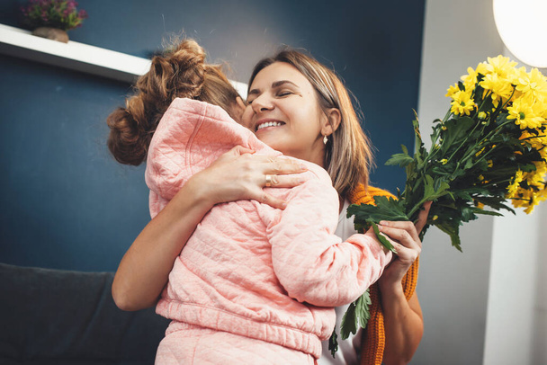 Blonde Mutter umarmt ihre Tochter, nachdem sie am Muttertag Blumen von ihr erhalten hat - Foto, Bild
