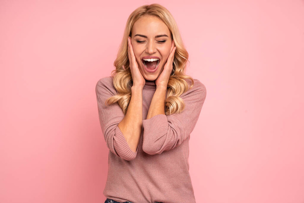 Portrait of beautiful joyous woman screaming and gesturing as winner isolated over pink background in studio. - 写真・画像