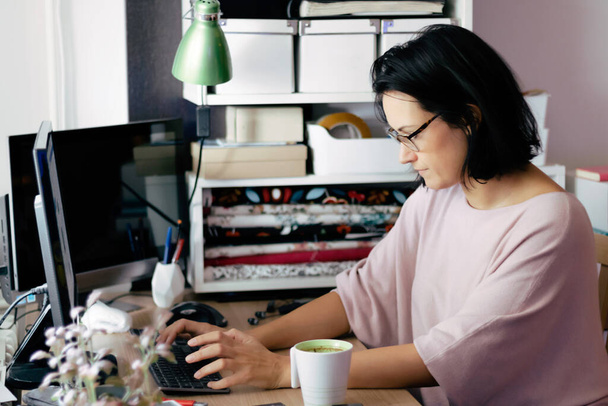Midden volwassen vrouw met behulp van desktop PC tijdens het werken vorm thuis. - Foto, afbeelding