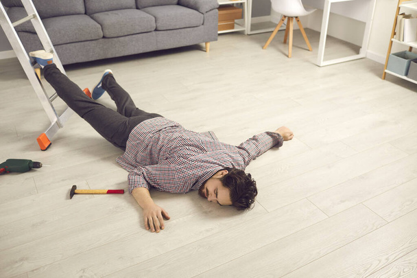 Молодой человек, который упал с лестницы во время ремонта дома, лежа без сознания на полу - Фото, изображение