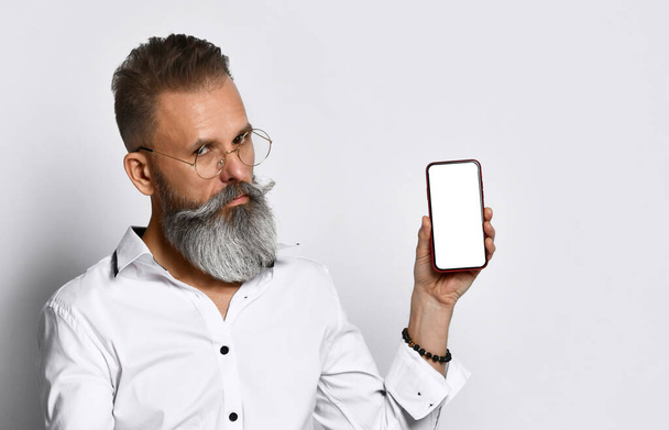 Hipster man with glasses shows the phone to the camera and confidently smiling. - Φωτογραφία, εικόνα