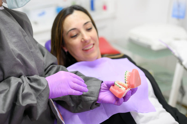 Zubař ukazující pacientovi zubní model ortodoncie, vysvětlující pacientovi ortodontickou léčbu na zubní klinice. - Fotografie, Obrázek