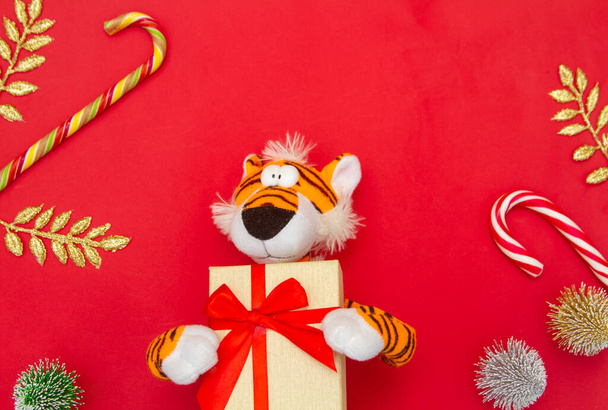 Jahr des Tigers 2022, Spielzeugtiger, der ein Geschenk mit roter Schleife auf leuchtend rotem Hintergrund hält, Urlaubskonzept, Stofftier. - Foto, Bild