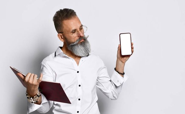 Hipster man in eyewear with notebook showing smartphone - Photo, image