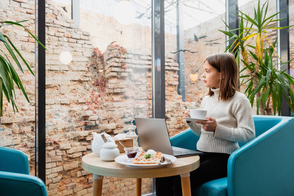 Menina com uma xícara e laptop em uma mesa em um café. - Foto, Imagem
