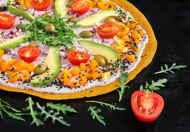 Delicious raw pizza with avocado, pepper, arugula, olives and tomatoes on a black background. - Fotografie, Obrázek