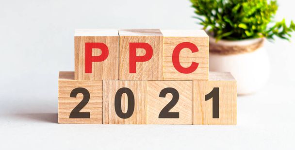 白いテーブルの上に木製のブロックによって形成された単語PPC 2021 。フロントビューのコンセプト、背景の花. - 写真・画像