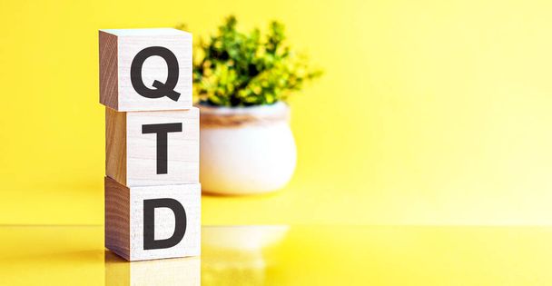Motivatív szavak: QTD 3D-s fából készült ábécé betűkkel, élénk sárga háttérrel, másolási hellyel, üzleti koncepcióval. Elülső nézet fogalmak, virág a háttérben. - Fotó, kép